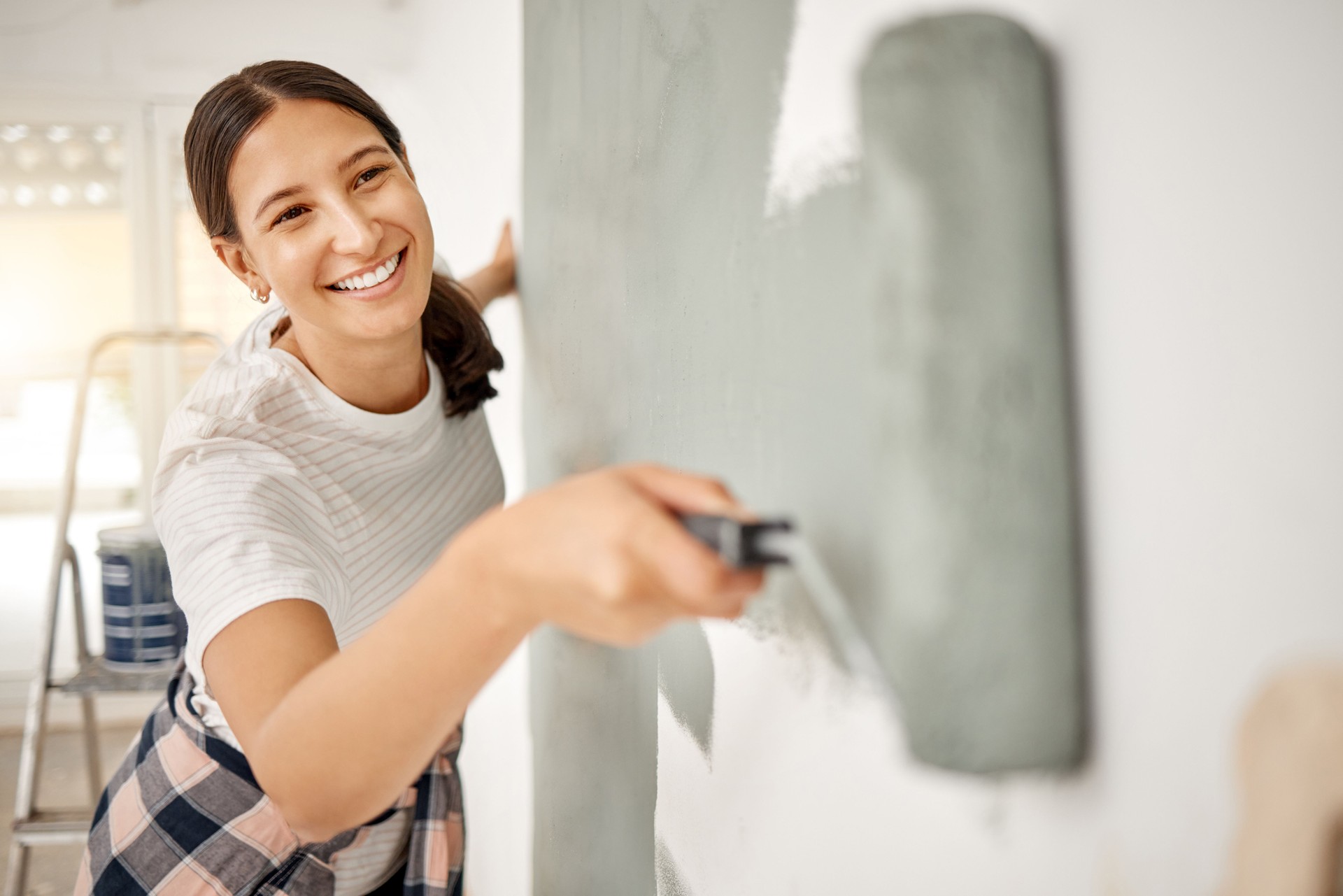 Shot of a beautiful young woman painting a wall at home